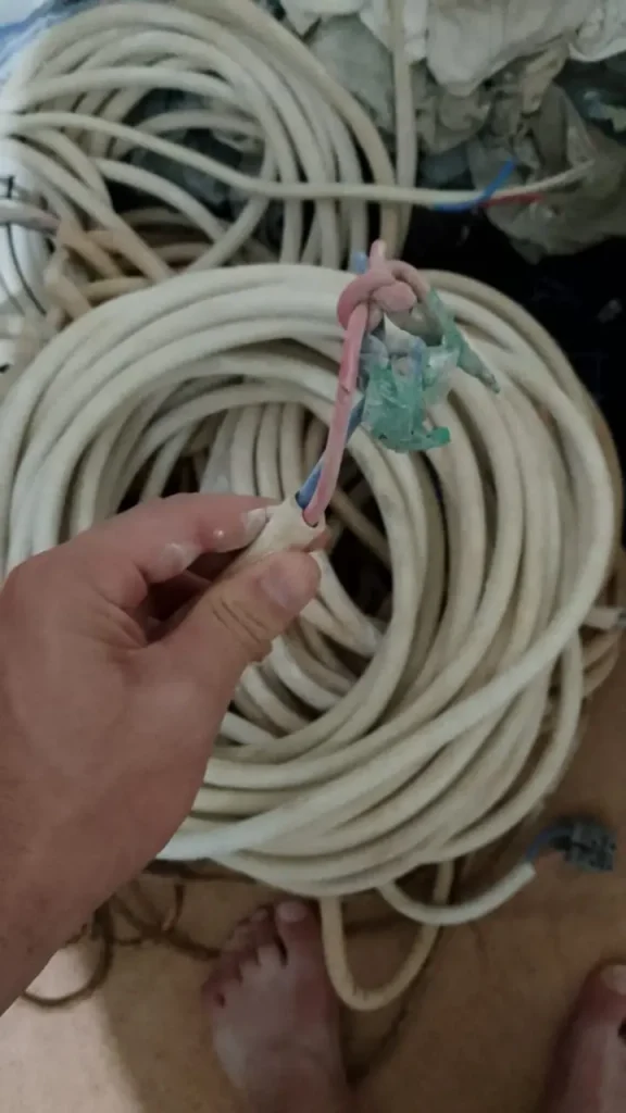 Hand holding a piece of insulated scrap cable showing internal copper wires before sale to buyers in Makkah
